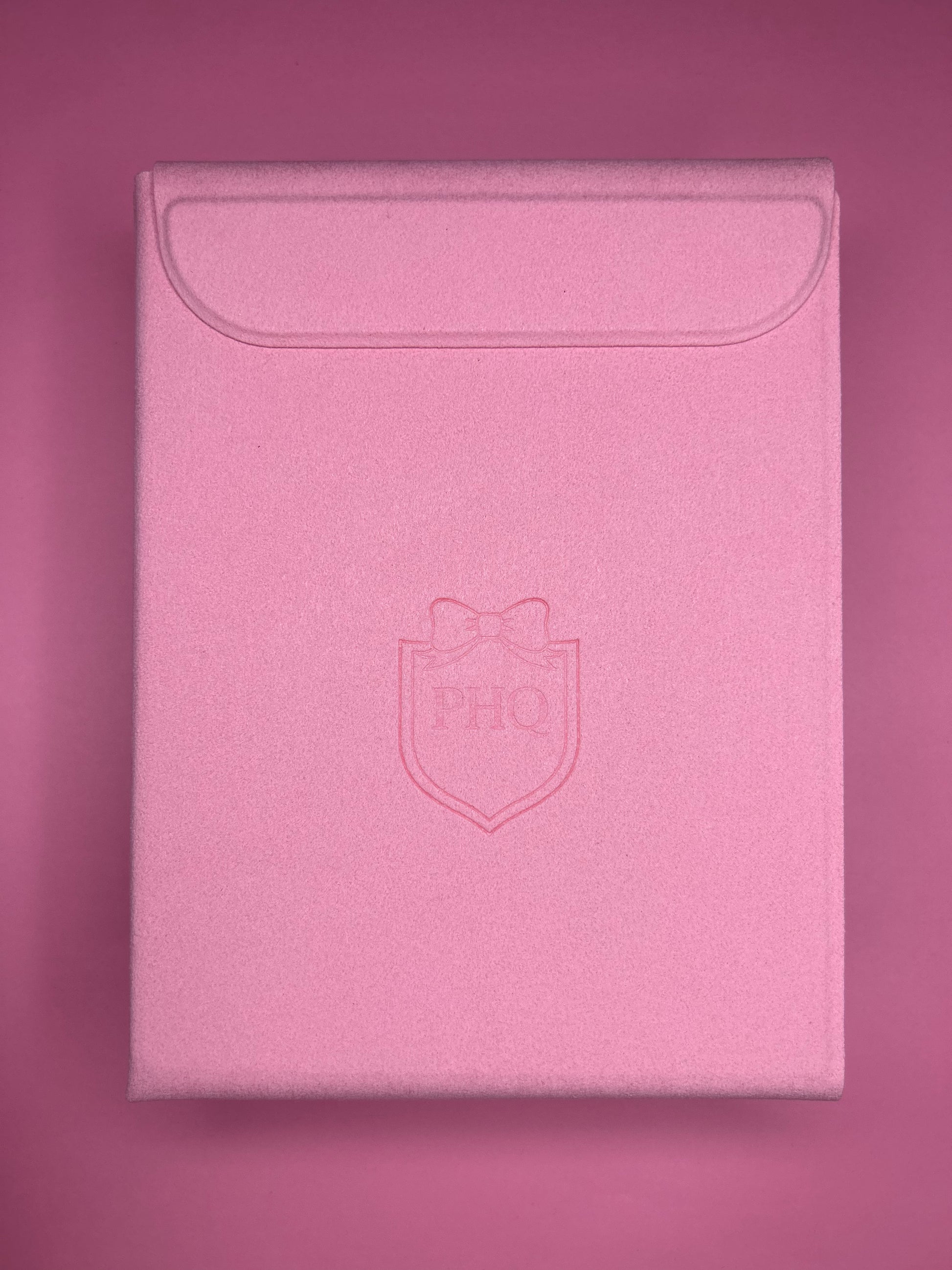 Pink PoutHQ textured envelope-style pouch with a flap closure and an embossed PHQ bow shield logo on the front, set against a matching pink background.